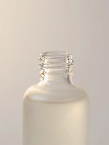 Macro close-up of translucent skincare bottle reflecting soft morning light, pearlescent background, dreamy editorial