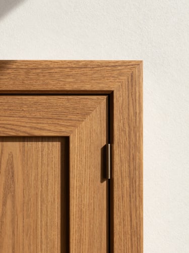 Extreme close-up of a bespoke oak cabinet door reveal, north-facing daylight raking across the grain, the hairline seam between panel and frame razor-sharp, warm wood tones against a linen-white wall — architectural framing, no people