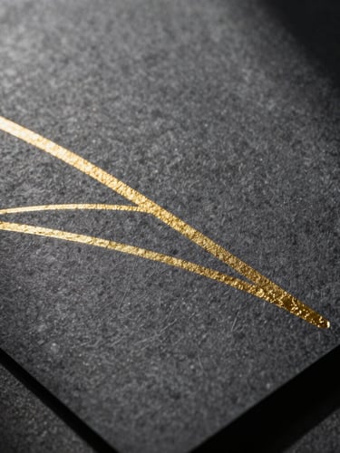 Extreme close-up of heavy-weight dark graphite paper with debossed gold leaf lines, dramatic side lighting casting deep shadows, luxurious physical texture.
