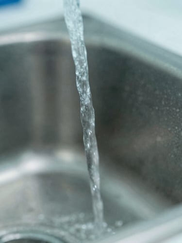 Close-up of clean water jets spraying onto a stainless steel surface, showing clinical laboratory lighting, sharp focus, teal and slate gray tones, macro details