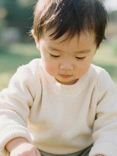 Candid lifestyle photo of a toddler playing in a sunny garden, wearing a soft cream knit sweater, warm natural daylight, shallow depth of field, 35mm film look