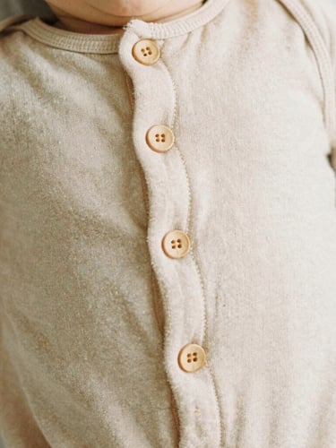Close-up of soft organic cotton baby romper with delicate wooden buttons, warm beige textile texture, soft natural light, 35mm film look