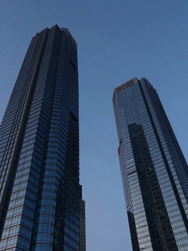 Low-angle architectural photography of Noida skyline during the blue hour, towering steel-and-glass skyscraper reflecting deep indigo sky, clean geometric lines