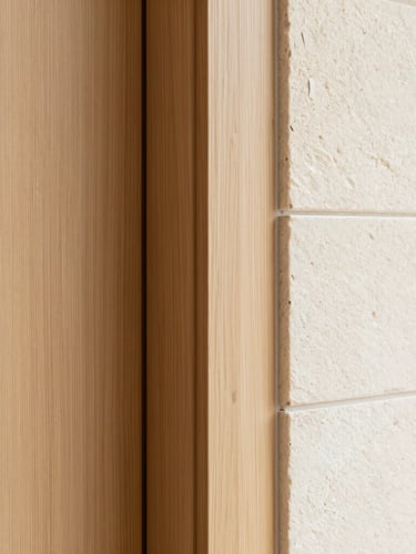 Close-up architectural photography of precise material joints, wood panel meeting a smooth natural stone wall, soft warm side lighting, sharp focus