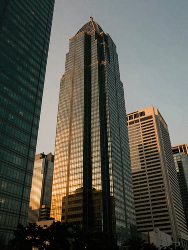 Dramatic low-key architectural wide angle of Jakarta's Sudirman central business district at golden hour, warm window light reflecting off glass towers, generous negative space.