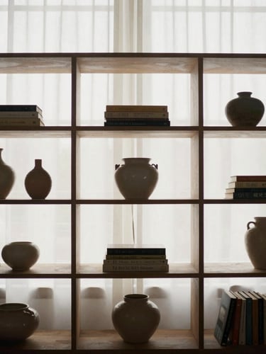 Medium crop of styled mid-century modular shelving holding books and small ceramic vessels, soft diffused morning window light