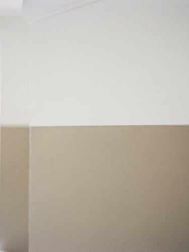 A sharp architectural crop of a perfectly taped, razor-sharp paint edge against a warm putty wall, soft natural window light, 35mm photography