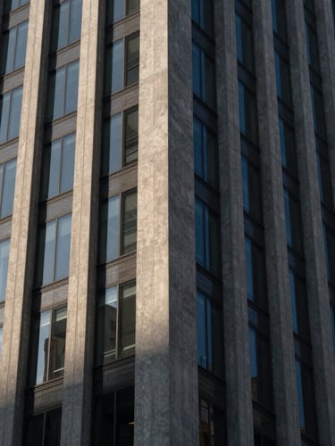 A sharp, high-contrast close-up of a modern concrete and steel skyscraper facade, dramatic architectural shadows, cool ambient twilight light.