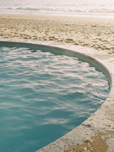 Warm editorial photography of a sun-drenched stone thermal pool with rippling water, soft morning daylight, minimalist composition, 35mm film