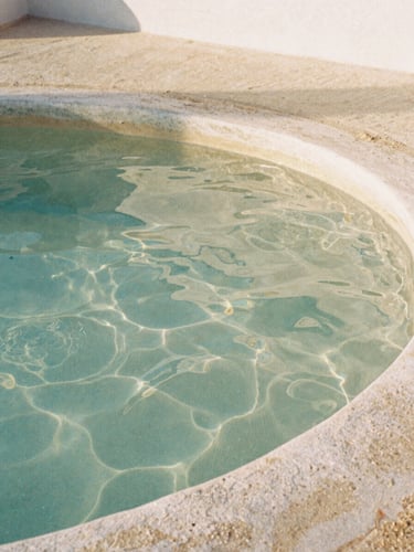 Extreme close-up of warm rippling thermal water in a stone pool, soft morning daylight filtering through, minimalist Mediterranean architecture, 35mm film style.