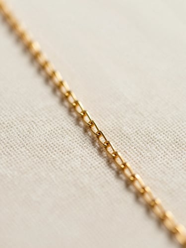 Extreme macro close-up of an ultra-fine gold-plated chain resting on a textured linen surface, soft diffused daylight, shallow depth of field