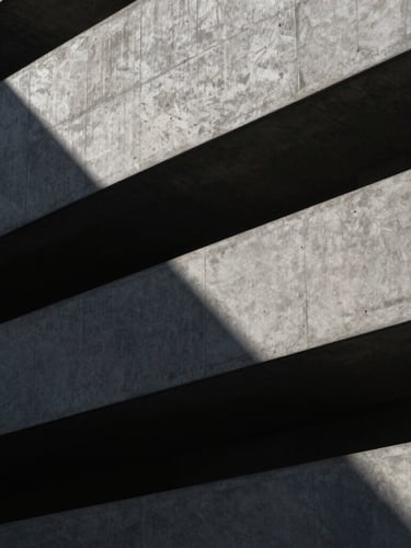 Low-key, high-contrast architectural crop of a modern concrete facade with sharp geometric shadows, cool tones, clean lines.