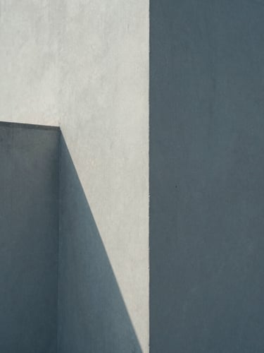 A minimalist, close-up photograph of architectural concrete angles casting clean geometric shadows under soft, diffused north-facing daylight.
