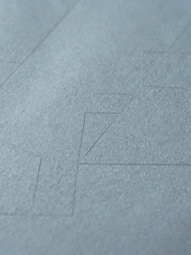 Extreme close-up of fine textured cotton paper with deep debossed geometric lines, soft daylight casting subtle shadows across the surface, minimalist editorial composition, 35mm.