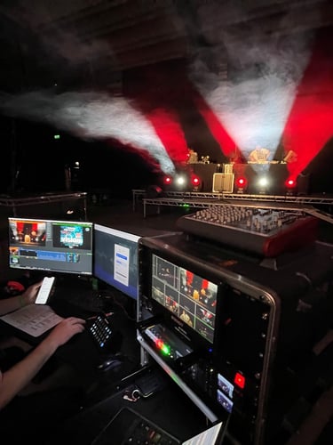 Video production technician managing a live stream event broadcast from a dark stage with red and white lighting.