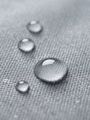 Macro close-up of water droplets repelling off a clean, stone-gray technical fabric surface, bright clinical lighting, sharp focus on the weave structure.