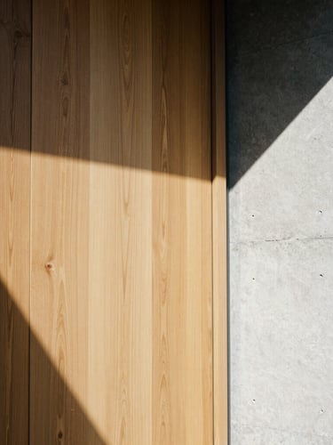 Portrait architectural film photography showing a tight detail crop of grain-matched oak panels meeting a polished concrete wall, sharp sunlight and high-contrast geometric shadows