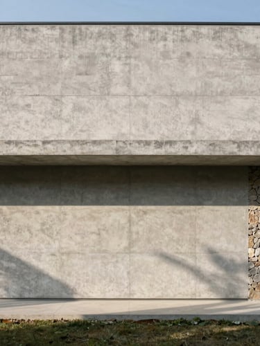 Wide-angle architectural photograph of a minimalist concrete house facade, sharp natural daylight casting long geometric shadows, native stone accents, 35mm lens.