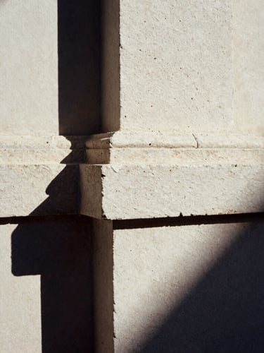Close-up of hand-chiseled basalt stone junction meeting raw plaster, harsh high-contrast morning sunlight, deep shadows, 35mm film