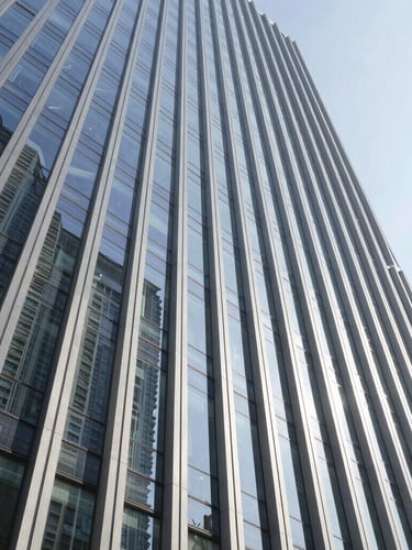 Wide-angle architectural shot of a modern vertical high-rise facade under crisp daylight, showcasing flawless structural glass joints and clean steel lines with sharp geometric shadows.