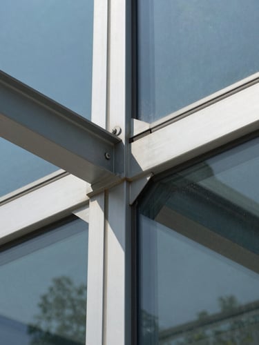 Macro detail shot of a structural glass connection on a commercial building, focusing on clean steel joints, flawless glass panels, and sharp geometric shadows under bright daylight.