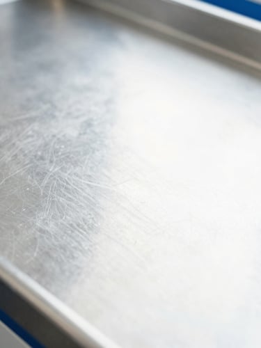 Macro detail shot of a clean stainless steel workspace surface, bright high-key daylight, cool whites, sharp focus, 35mm