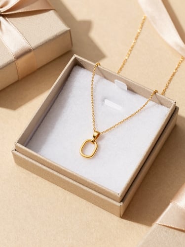 Overhead flat lay of elegant jewelry gift packaging on a soft sand-beige surface, featuring a gold-plated necklace nestled inside a premium custom box with delicate ribbon.