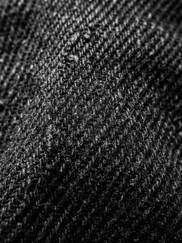 Extreme close-up of heavy black cotton fabric texture, stark studio lighting, high-contrast, sharp shadows, brutalist composition, 35mm film grain
