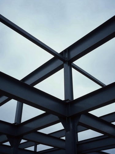Low-angle heroic shot of structural steel frameworks against a dramatic cool overcast sky, industrial scale, 35mm film