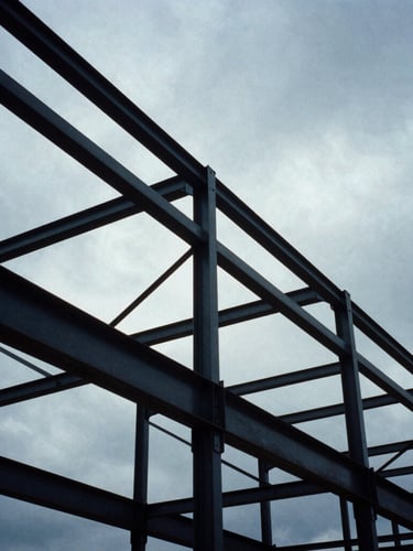 Low-angle heroic shot of massive structural steel frameworks against a dramatic overcast sky, cool industrial tones, 35mm film.