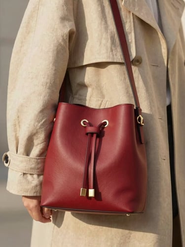 Close-up of a model in a beige linen trench coat holding a cherry-red bucket bag, soft natural afternoon light, 35mm style.