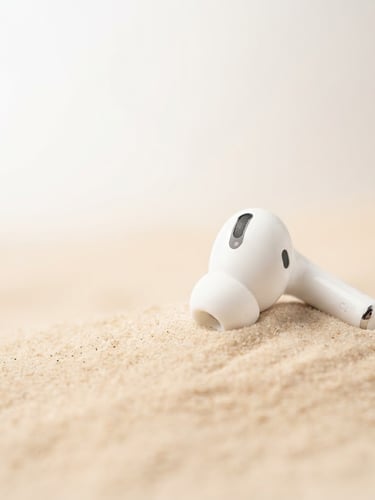 Premium wireless earbuds on a soft beige desert background, crisp studio light, 3/4 angle, ample negative space to the left