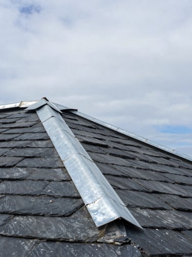 Low-angle architectural shot of a slate roof with hand-beaten zinc joints meeting a dramatic coastal sky, bright overcast daylight, sharp focus
