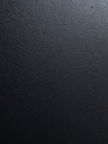 Extreme close-up of a freshly cured matte black textured powder-coated steel surface, showing fine physical grains under dramatic directional lighting.