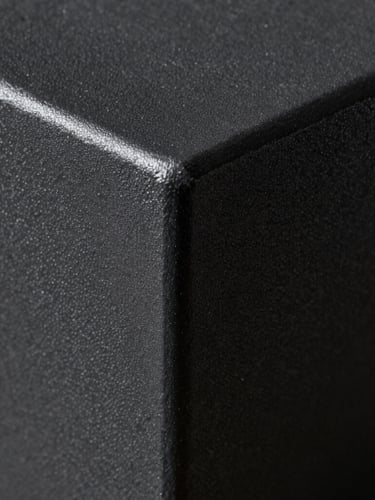 Macro shot of a freshly cured textured matte black powder-coated steel component, dramatic directional light catching the micro-texture, deep iron-grey shadows.