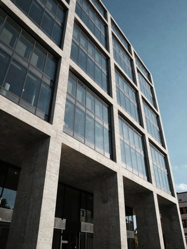 Wide-angle architectural detail of a modern concrete and glass infrastructure building in Madrid, high-contrast daylight, deep cool shadows.