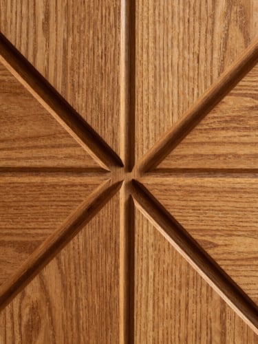 Macro side-lit shot of deeply routed geometric timber panel, sharp shadow-defining channels, amber-lit oak grain