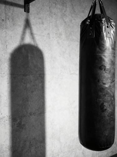 Black and white portrait shot of an empty gym corner with a single punching bag, high contrast, rough concrete wall, sharp focus, side lighting creating a dramatic shadow.