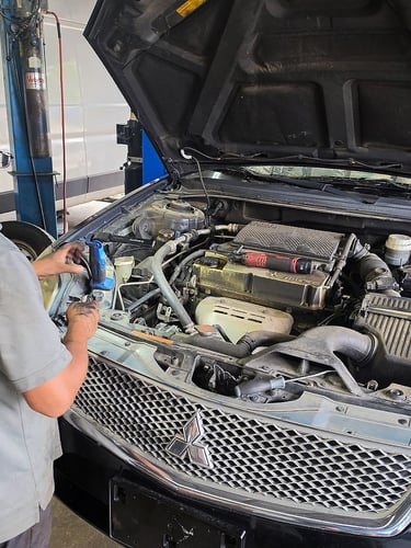 Professional auto mechanic inspecting a Mitsubishi car engine for repair at a garage.