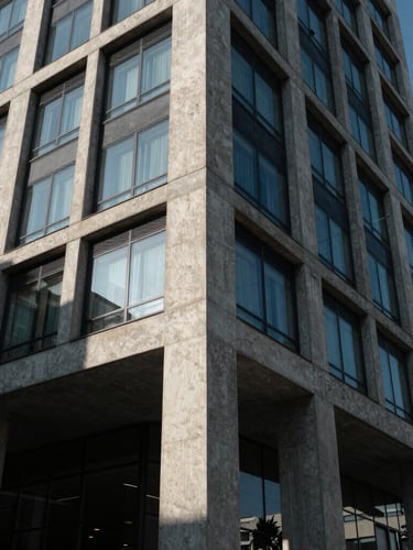 Low-angle architectural photograph of a modern concrete and glass building facade in Bakırköy, high-contrast morning light casting sharp geometric shadows, raw material textures visible.