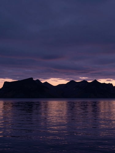 Horizonte minimalista al crepúsculo en Islandia, cielo oscuro con tonos índigo, siluetas de montañas lejanas y agua calma reflejando la última luz.