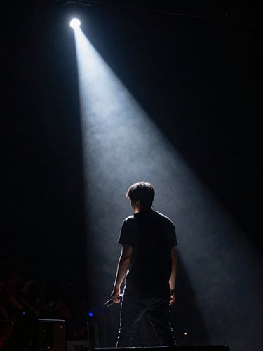 Raw concert energy captured in low light, a silhouette of a musician against a single piercing stage light cutting through absolute darkness.