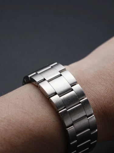 Macro close-up of a polished steel bracelet on a wrist, sharp studio lighting, deep shadows, minimalist dark background, 50mm
