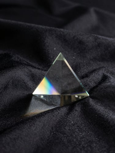 A glass prism catching a single beam of soft light, casting a subtle rainbow spectrum across a dark textured silk background, moody chiaroscuro lighting.
