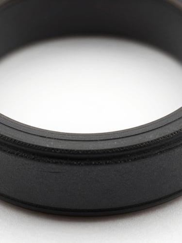 Macro studio photography of a custom-machined black elastomer O-ring showing dense material geometry and precise cross-section tolerances, high-contrast lighting.