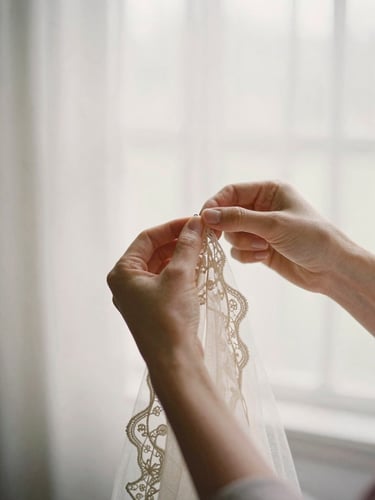 Hands carefully hand-sewing delicate lace onto tulle, soft diffused window light, romantic editorial photography