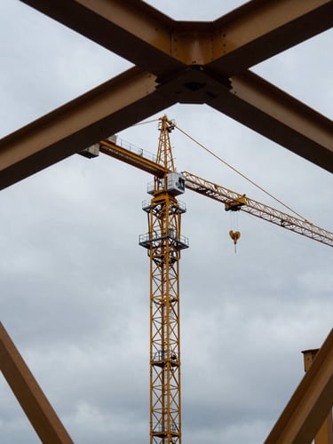 Low-angle dramatic shot of a yellow tower crane silhouetted against an overcast Baltic sky in Szczecin, structural steel trusses cutting the frame diagonally, industrial maritime atmosphere.