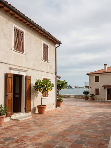Environmental wide shot of a northern Adriatic pension courtyard in overcast daylight — terracotta-tiled forecourt, painted wooden shutters, a potted lemon tree by the entrance, the building facade occupying the left half of the frame, lagoon glimpsed between buildings in the background, no people, available light