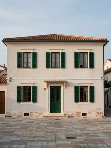 Environmental wide shot of a two-storey Adriatic pension building facade at street level, pale render exterior with green shutters, morning overcast light, stone pavement in foreground, no people, framed to show the building in its coastal town context