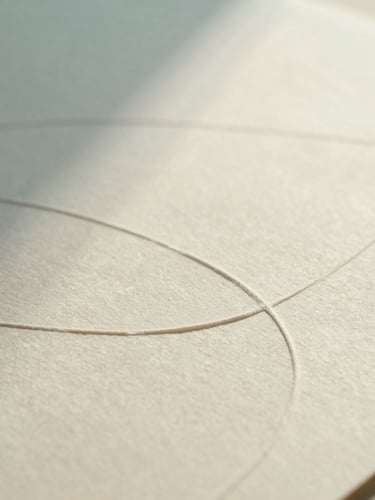 Close-up of tactile design materials on a warm cream surface, soft textured paper with embossed curved lines, diffused natural daylight, cool cyan shadows, shallow depth of field, minimalist abstract photography.